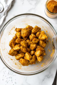 This image shows chicken being cut into bite-sized pieces and coated generously with turmeric.