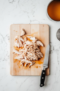 shred-the-cooked-chicken-breasts on chopping board with a knife