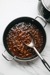 This image shows a pan being deglazed with liquid, scraping up browned bits to create a rich base for the soup.