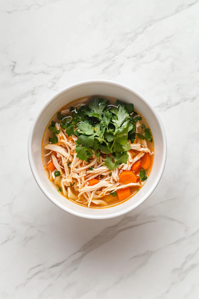 Slow-cooker chicken noodle soup served in a white bowl with shredded chicken and cilantro