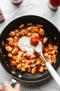 This image shows heavy cream being mixed with chicken in the skillet until almost fully cooked.