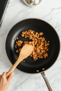 This image shows minced garlic being stirred into the skillet with caramelized onions, adding an aromatic touch just before the heat is turned off.