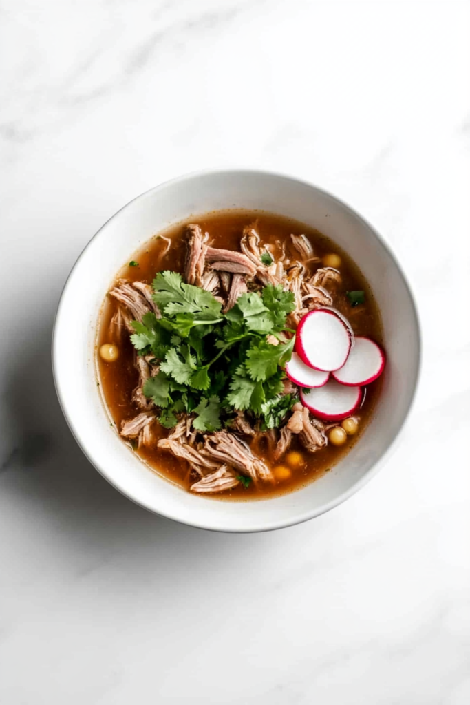 A vibrant bowl of Easy Pork Posole garnished with fresh cilantro leaves and thinly sliced onions, showcasing a traditional and hearty Mexican soup.