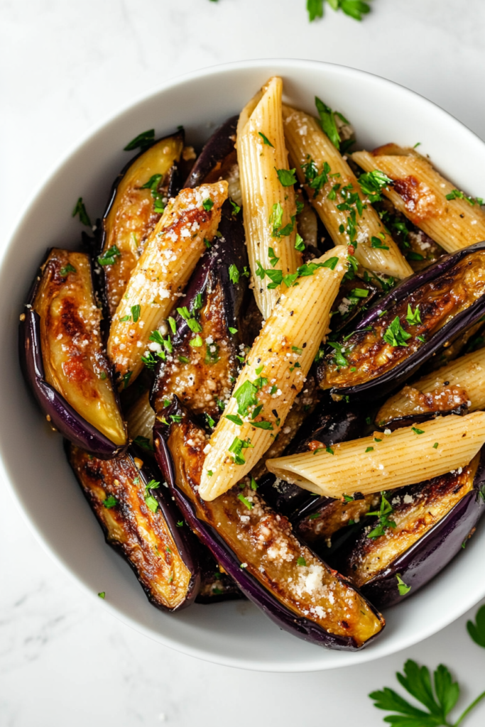 This image shows garlic eggplant penne pasta served in a white bowl, topped with shredded cheese and garnished with fresh cilantro.