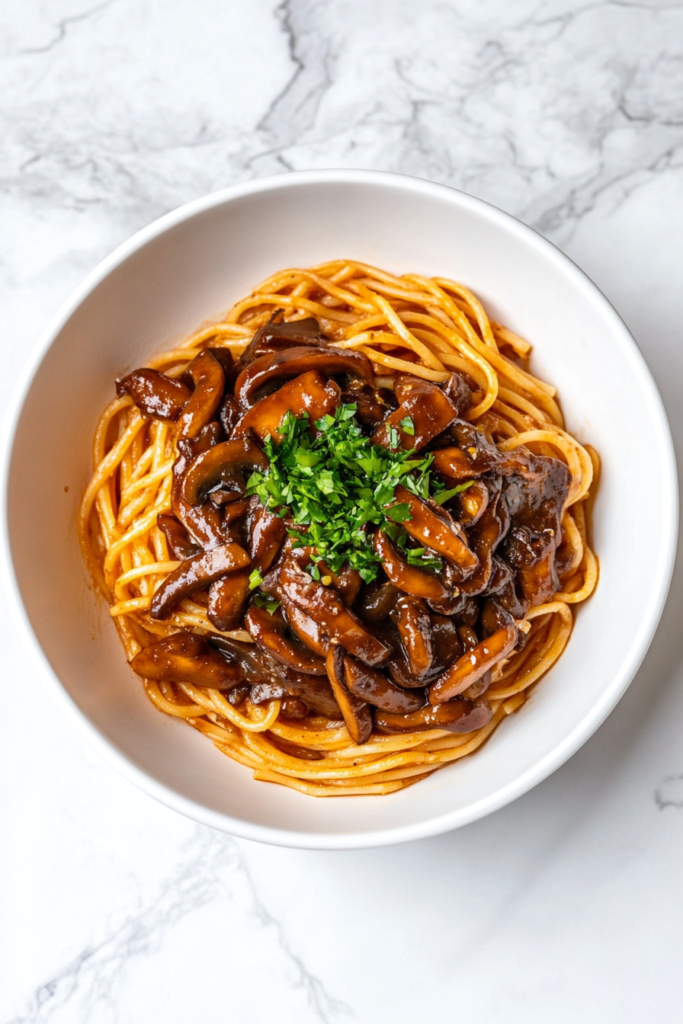 This image shows mushroom spaghetti aglio olio served on a white round plate, drizzled with sauce and garnished with cilantro.