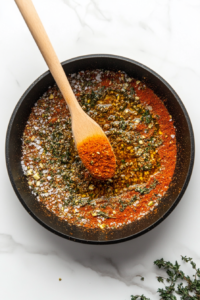 This image shows Cajun spices and olive oil being added to a heated skillet to create a flavorful base for cooking the shrimp.