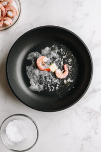 This image shows raw shrimp added to a hot skillet with melted butter, preparing to be cooked to a perfect golden and juicy texture.