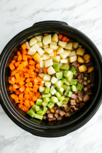 This image shows fresh carrots and potatoes being layered over the seasoned chuck roast in the slow cooker, forming the perfect mix of meat and vegetables for the pot roast.