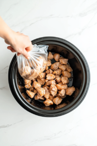 This image shows coated chicken pieces being carefully transferred into the slow cooker for Crockpot Orange Chicken.