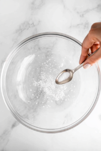 This image shows cream of tartar being added to the drained chickpea liquid to help stabilize the whipped cream during the whipping process.