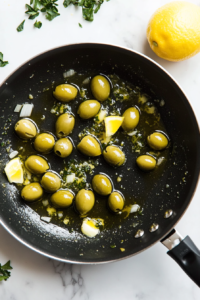 this image shows Lemon juice being poured into a pan of sautéed olives and garlic, adding a zesty flavor to the Vegan Green Olive Pasta Sauce.