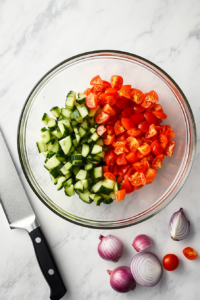 This image shows a mix of chopped vegetables, such as cucumbers and tomatoes, being added to a bowl, the first step in creating a vibrant Keto Greek Cucumber Salad.