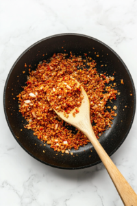 this image shows Minced garlic being added to a skillet with sautéed onions, enhancing the aroma and flavor of the vegan mushroom stroganoff base.