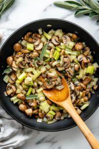 This image shows fresh garlic and sage being added to the sautéed vegetables, infusing the mixture with aromatic flavors for the casserole.