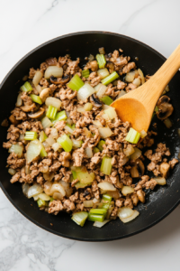 This image shows ground turkey being added to the skillet with vegetables and seasonings, forming the filling for the casserole.