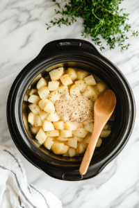 This image shows hashbrowns, seasonings, and other ingredients being added to the crockpot, starting the preparation for a creamy potato soup.