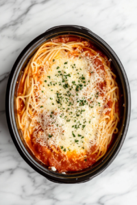 This image shows marinara sauce being poured and spread over the cheese layer in the slow cooker, preparing for the next lasagna layer.