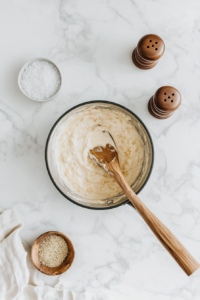 This image shows ground nutmeg, freshly cracked pepper, and a pinch of salt being sprinkled into the béchamel sauce, enhancing its rich and aromatic flavor profile.