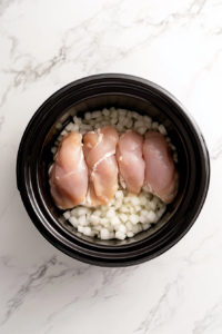 This image shows diced onions and seasoned chicken being added to a crockpot, starting the process of making creamy chicken and dumplings.