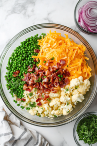 This image shows fresh peas and other ingredients, such as bacon and cheese, being added to a large mixing bowl as the base of the low-carb pea salad.