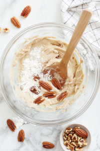 This image shows chopped pecans and raisins being folded into the banana bread batter for added texture and flavor.