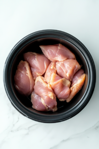 This image shows raw chicken breasts being placed in the slow cooker as the first step in preparing Crockpot Chicken Noodle Soup.