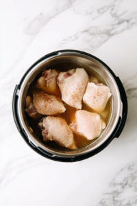 Raw chicken breasts coated with a savory seasoning mix being carefully placed into the Instant Pot, ready for cooking in a flavorful broth.