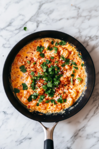 This image shows a skillet of shrimp and cream cheese being seasoned with spices and lime juice, infusing the dish with tangy and zesty flavors.