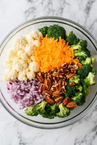 this image shows Cheddar cheese and raw pecan pieces sprinkled over the vegetables in the salad bowl.