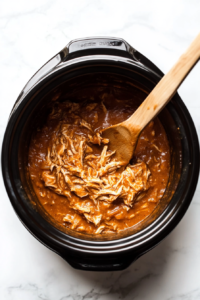 This image shows shredded chicken being added back into the slow cooker, mixing with the creamy chili base to complete the Crockpot White Chicken Chili.