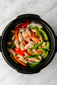 Adding sliced peppers and onions over chicken in the slow cooker