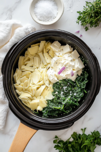 This image shows spinach, artichokes, shredded cheese, and sautéed vegetables being added to a slow cooker, beginning the preparation for creamy spinach artichoke dip.