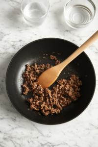 This image shows taco seasoning being mixed into cooked ground beef in a skillet, followed by simmering to infuse the flavors for Crockpot Enchiladas.