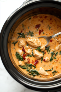 A spoon tasting the creamy Tuscan sauce while adjusting the seasoning with a dash of salt and pepper to enhance the dish’s flavor before serving.