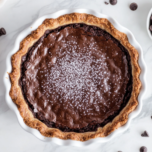 This image shows a delicious vegan brownie pie in a white serving dish, featuring a perfectly crispy golden brown gluten-free crust and a rich, fudgy chocolate filling, making it an irresistible dessert.