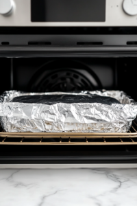 This image shows the baked loaf of no yeast bread being carefully taken out of the oven, with a golden crust visible on top.