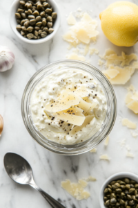 This image shows a blender mixing together garlic, lemon juice, Dijon mustard, Greek yogurt, and seasonings to create a smooth and creamy dressing for the shrimp Caesar salad.