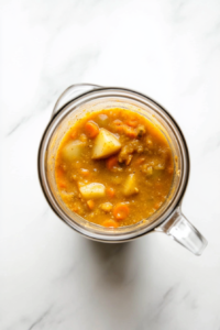 This image shows a blender filled with the cooked soup ingredients, being blended into a smooth and creamy consistency for the vegan broccoli cheese soup.