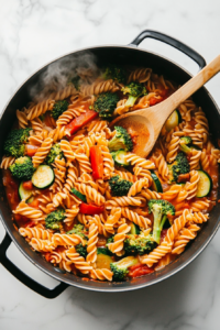 this image shows The mixture of pasta, vegetables, and red creamy sauce boiling on high heat in a large pot, ready to be reduced to low heat for 12 minutes to cook the pasta al dente.