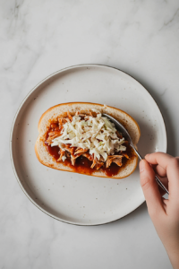 This image shows a fresh pulled pork sandwich being assembled, with tangy BBQ pork piled on a bun and topped with creamy coleslaw.