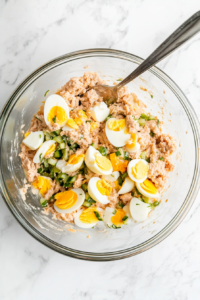 this image shows Diced boiled eggs being gently folded into the tuna salad mixture, ensuring even incorporation without breaking the delicate pieces.