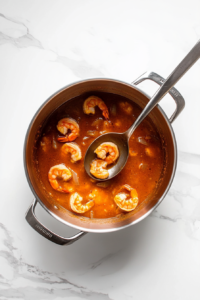 this image shows A spoon stirring the shrimp in the pot to ensure even cooking and distribution of seasoning.