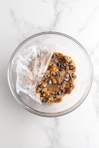 wrapped portion of salted caramel cookie dough resting in the refrigerator, chilling to ensure the cookies bake with the perfect texture and flavor.