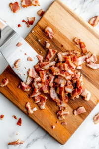 This image shows strips of crispy cooked bacon being chopped into bite-sized pieces on a cutting board to add to the carnivore chicken salad.