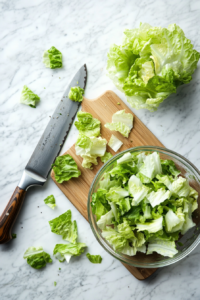 This image shows fresh romaine lettuce being chopped into bite-sized pieces, forming the base of the shrimp Caesar salad.