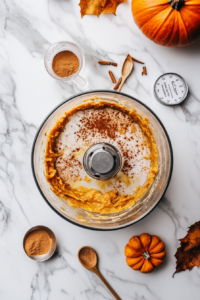 This image shows organic pumpkin purée, arrowroot powder, maple syrup, and warm spices being blended together in a bowl to create a rich, velvety filling for the pumpkin pie.