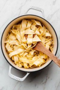 This image shows egg noodles being cooked in a pot of boiling water, ensuring they are ready to be added to the soup.