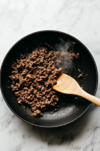 This image shows ground beef being cooked in a skillet, the first step in preparing the filling for Crockpot Enchiladas.