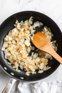 This image shows a top-down shot of onions being cooked in a pan, caramelizing to bring out their sweet, rich flavor for French Onion Soup.