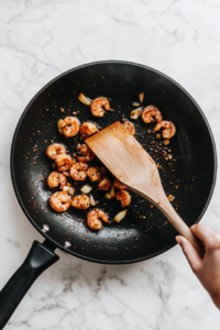 This image shows seasoned shrimp being stir-fried in a skillet with coconut oil, cooking until they turn pink and tender, ready to be combined with the pasta and sauce.